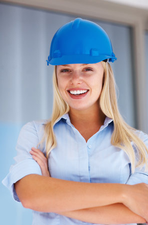 Female architect standing with hands folded. Portrait of female architect wearing blue helmet and smiling.の写真素材
