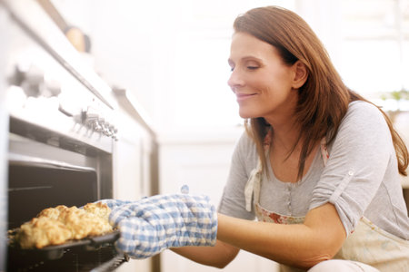 Enjoying the aroma of her fresh scones. A mature woman taking scones out from the oven.の写真素材