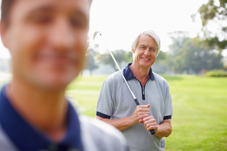 Senior man holding a golf club and smiling. Portrait of senior man holding a golf club and smiling with son in foreground.の写真素材