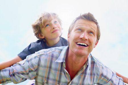 Cheerful mature man with his son having fun together against sky. Portrait of a cheerful mature man with his son having fun together against sky.の写真素材