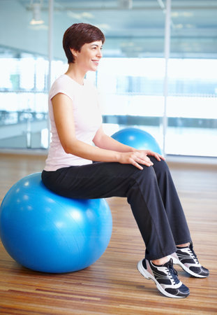 Woman sitting on gymnastic ball. Full length of woman sitting on gymnastic ball and smiling.の写真素材