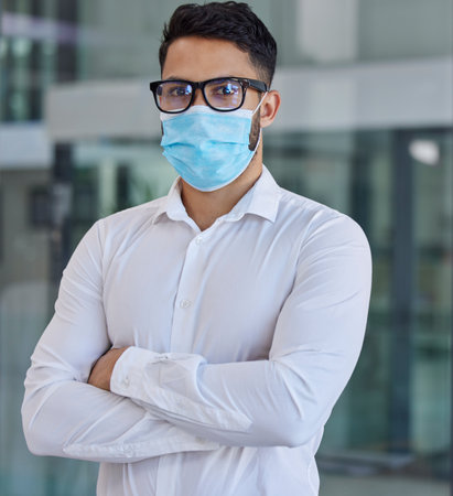Businessman, mask and glasses with arms crossed in covid vision for health, safety and protection at office. Portrait of confident employee man in healthcare management during pandemic at workplaceの写真素材