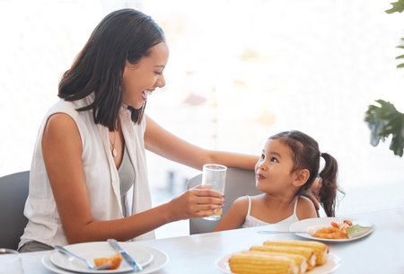 Woman, food and eating at home for health, wellness and diet nutrition at the dining table. Meal, lunch and mother and daughter eat and drink juice together for hungry child in the family homeの写真素材