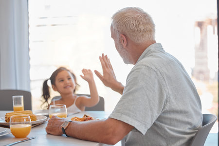 High five, breakfast and family with a girl and grandfather sitting at a dining room table for eating food. Motivation, health and children with a senior man encouraging his grandchild to eat healthyの写真素材