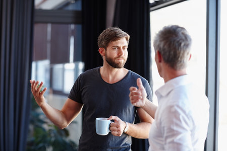 Getting down to some serious conversation. two handsome businessmen having a discussion in the office.の写真素材
