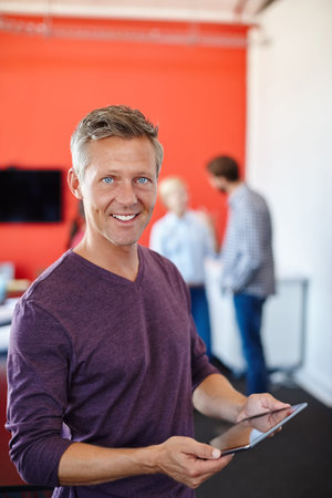 This tablet has made working so much easier. a handsome designer using a tablet with his coworkers...