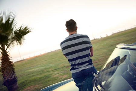 Better things are coming. Rearview shot of a man looking at the view while leaning against his car.の写真素材
