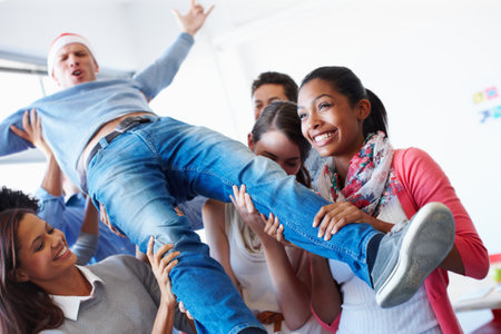 Christmas, office and party by business people silly, fun and happy in celebrating holiday, crowdsurf and joy. Festive, event and employee group with diversity lifting man in celebration of successの写真素材