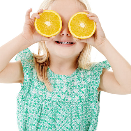 Healthy equals happy. Studio shot of a cute little girl playfully covering her eyes with oranges against a white background.の写真素材