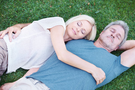 Intimacy and bliss. A mature couple lying on the grass and looking up at you happily.の写真素材