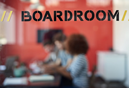Brainstorming session behind those doors. Closeup shot of a sign on a boardroom window with businesspeople blurred in the background.の写真素材