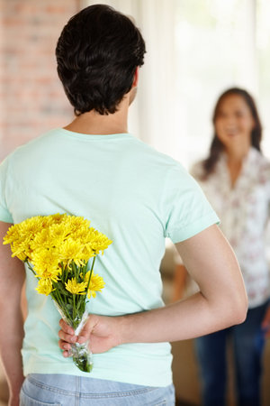 Remembering their anniversary...A young woman being surprised by her boyfriend holding a bunch of flowers behind his back.の写真素材