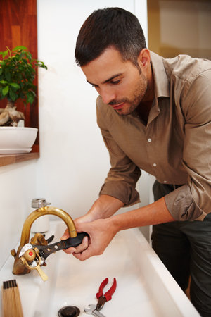 Hes Mr Fix-it. an attractive young man fixing the tap of a basin.の写真素材