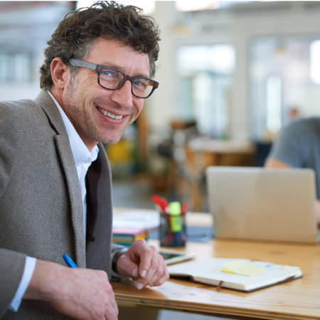 Setting the bar as a leader. Portrait of a smiling businessman sitting at his desk in a large office.の写真素材