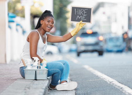 Woman, street and poster for looking for job or hiring for cleaning service, work or opportunity in city. Black woman, cleaner or domestic freelancer on metro sidewalk with basket, sign or productの写真素材