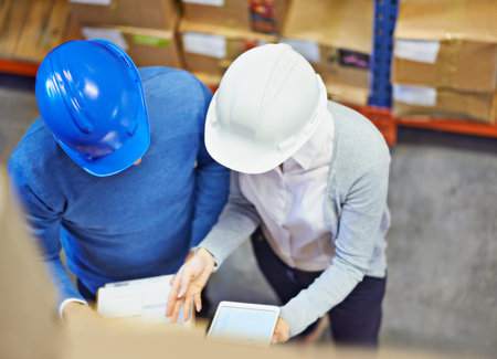 Factory managers. Overhead shot of two people wearing hardhats working in a warehouse.