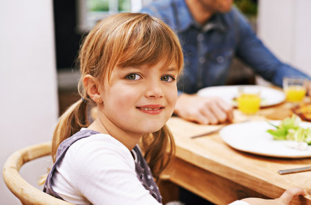 Family dinner is my favorite time of the day. A little girl sitting at the dinner table.の写真素材
