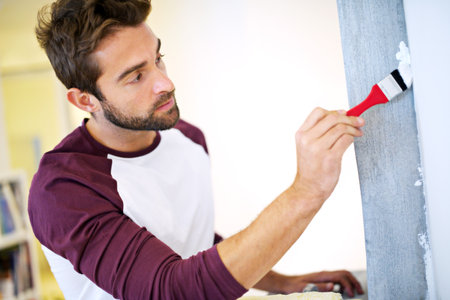 Using the correct brush is key. a young man painting a wall indoors.の写真素材
