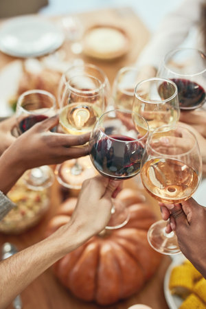 Wine, cheers and glasses at christmas toast, holiday celebration with food, friends and family together. Hands, wine glasses and friendship, celebrate diversity at dinner party with men and women.の写真素材