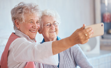 Phone, selfie and elderly friends smile for pictures to share on social media online while relaxing in retirement. Happy, love and senior women smiling while enjoy quality time at home in Berlinの写真素材