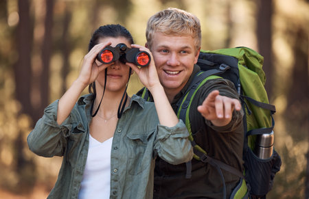 Couple, binoculars and pointing while hiking in nature, travel or outdoors vacation, holiday or trip. Freedom, man and woman on adventure, sightseeing or trekking and looking with field glasses.の写真素材
