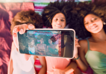 Woman, friends and phone for group selfie, summer and relax for friendship traveling or vacation together. Happy women relaxing lying on beach towels smiling for photo holding smartphone with displayの写真素材