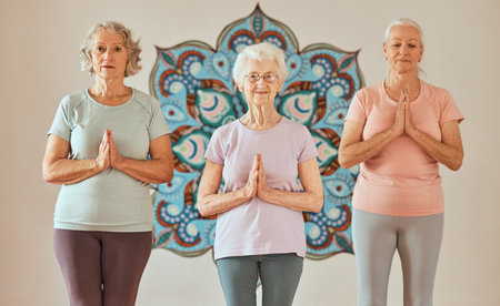 Senior, women and meditation with yoga and prayer pose for chakra balance and peace in fitness studio wall. Portrait of elderly yogi people, positive energy and wellness with zen, health and mandala.の写真素材