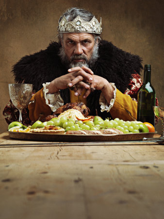 He feasts while the serfs starve. A mature king feasting alone in a banquet hall.の写真素材