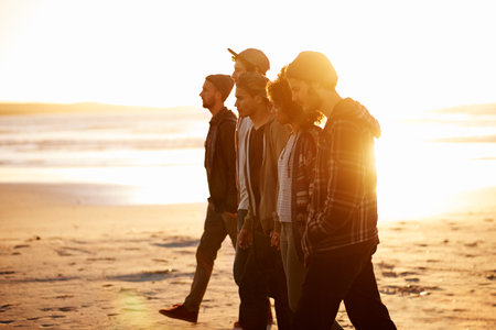 Heading for their next mission. a group of friends walking along a beach at sunset.の写真素材