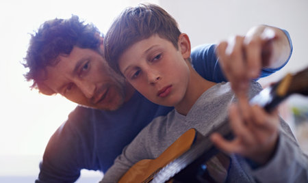 Perfect bonding activity. a boy learning to play guitar from his father.の写真素材