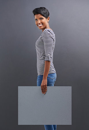 Your copyspace is in safe hands. Studio shot of a beautiful young woman holding a blank placard against a grey background.の写真素材