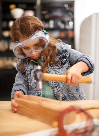 One of her many hobbies. a little girl hammering nails into a block of wood.の写真素材