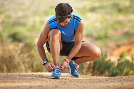 Fitness, shoes and man prepare before running in nature for health, wellness and exercise. Shoes, tying laces and getting ready with athletic man preparing for workout, training and jog or hikeの写真素材