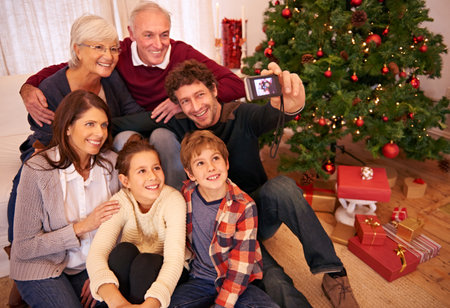 Family, christmas party and phone selfie, festive season or holiday celebration. Portrait, smile and grandparents, kids and parents celebrate, picture pose or photo smile for memory together in homeの写真素材