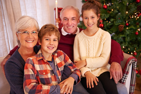 Christmas, senior couple and couch with grandchildren, happiness and relax for festive season at home. Xmas, love and elderly man with mature woman, grandkids or happy with smile, content or portraitの写真素材