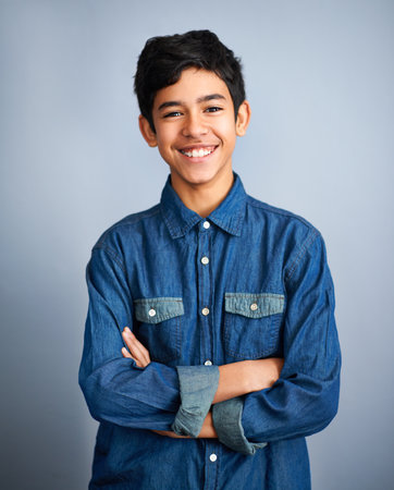 This kids got confidence. A cute young preteen boy standing and smiling against a grey background.の写真素材