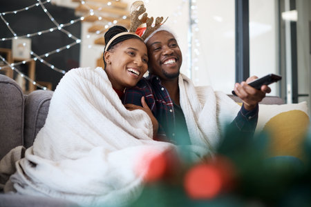 Christmas, comfort and African couple watching tv, news or a movie from the living room sofa. Television, relax and black man and woman on the couch for a film on a subscription service for festiveの写真素材