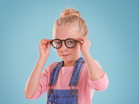 Looking smart and feeling sharp. Studio shot of a little girl wearing hipster glasses on a blue background.の写真素材