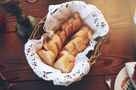 Bread, food and basket with a starter serving on a wooden dinner table in a home for a celebration event. Party, lunch and mutrition with a baguette on a surface for eating, dining or a mealの写真素材
