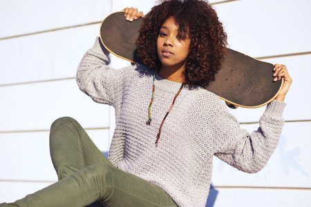 Ive always got my board with me. a young woman sitting with her skateboard in a skatepark.
