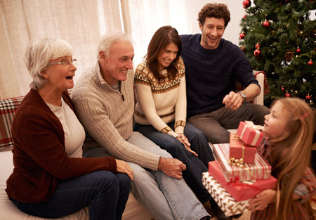 Christmas, happy family and child with a gift for excited grandparents at home on a winter holiday celebration. Wow, mother and father with a young girl kid giving present boxes to old man and womanの写真素材