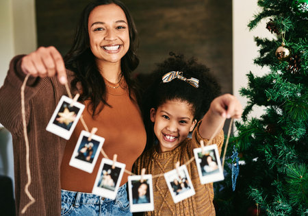 Christmas, decoration and mother and girl with Polaroid on a tree for love, happiness and celebration of holiday in a house. Festive, happy and portrait of a mom and child show picture for decoratingの写真素材
