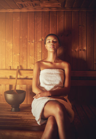 Sitting in the sauna. a young woman relaxing in the sauna at a spa.の写真素材