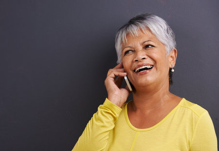 Can you hear me now. a mature woman talking on a mobile phone in a studio.の写真素材