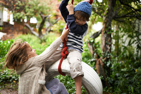 Tarzan and Jane. two cute kids playing on a tire swing in their garden.