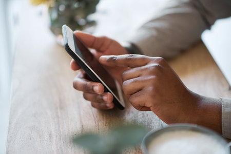 Hand, table and phone with a man browsing the internet online ot texting a mobile contact while...