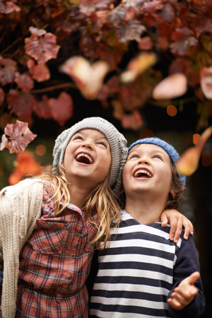 Autumn joy. Two cute kids lauging joyfully while watching Autumn leaves falling from the trees.