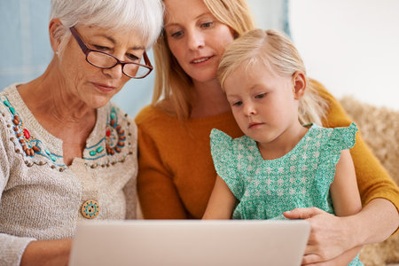 Learning about technology together. a young woman, her mother and her daughter sitting with a laptop indoors.の写真素材