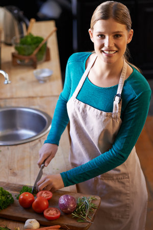 I love my veggies. Portrait of an attractive young woman chopping vegetables in the kitchen.の写真素材