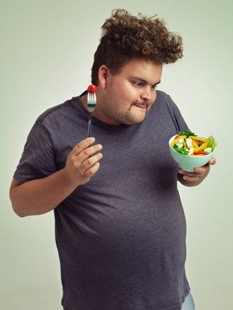 Excited about this salad. Studio shot of an overweight man holding a bowl of salad.の写真素材